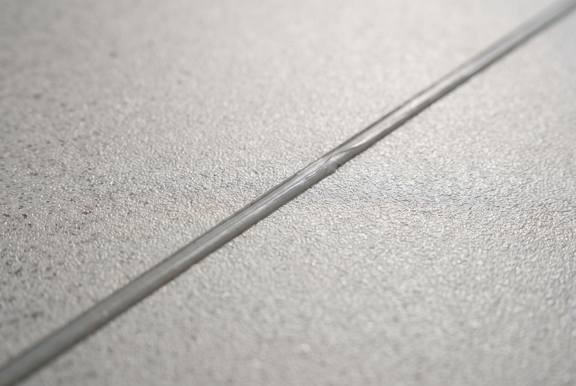 Close-up of a heat-welded seam sitting flush in grey speckled sheet vinyl