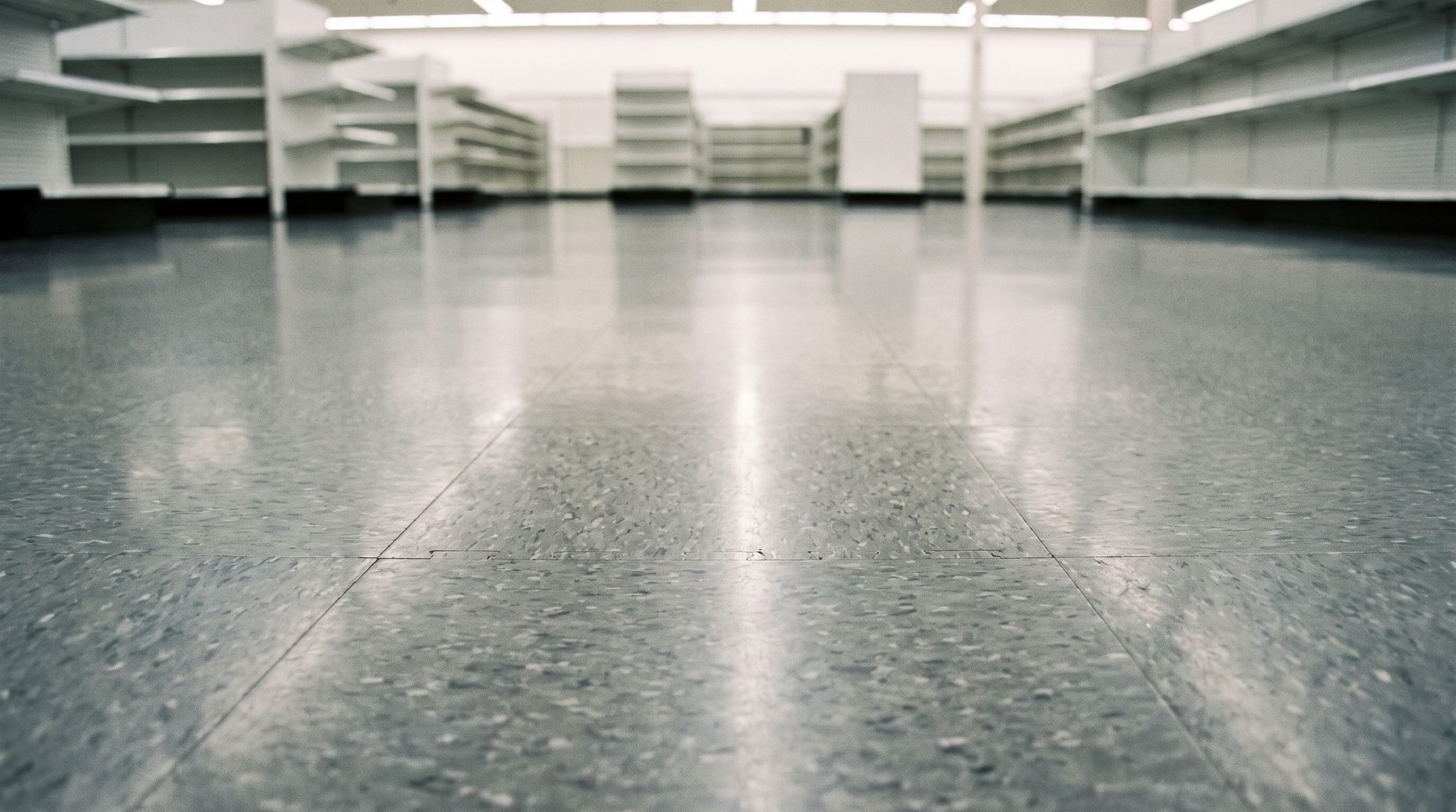 A large empty shop floor of grey interlocking vinyl tiles