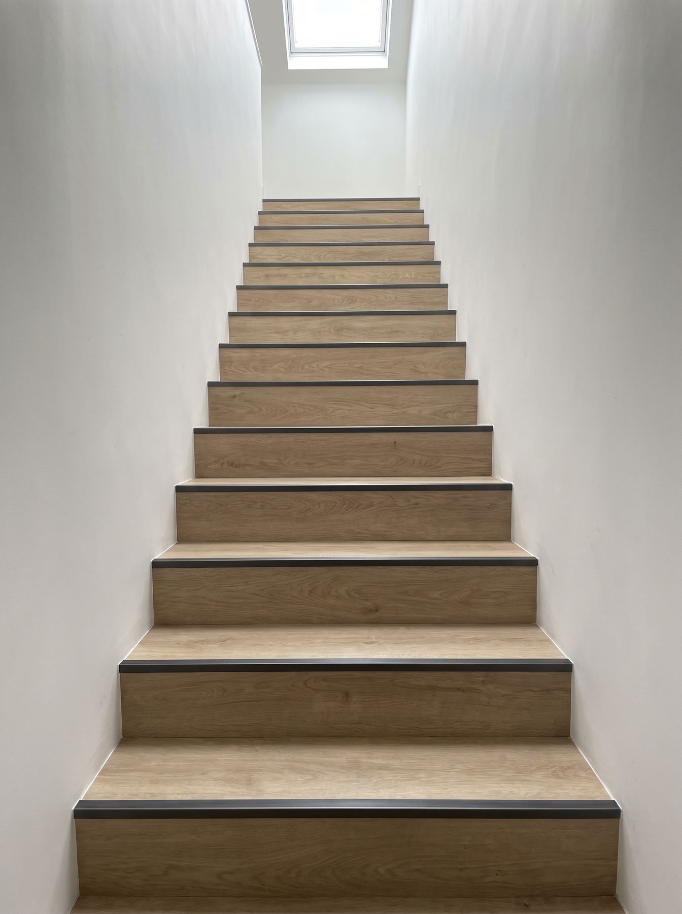 A staircase finished in light oak vinyl with dark stair nosings