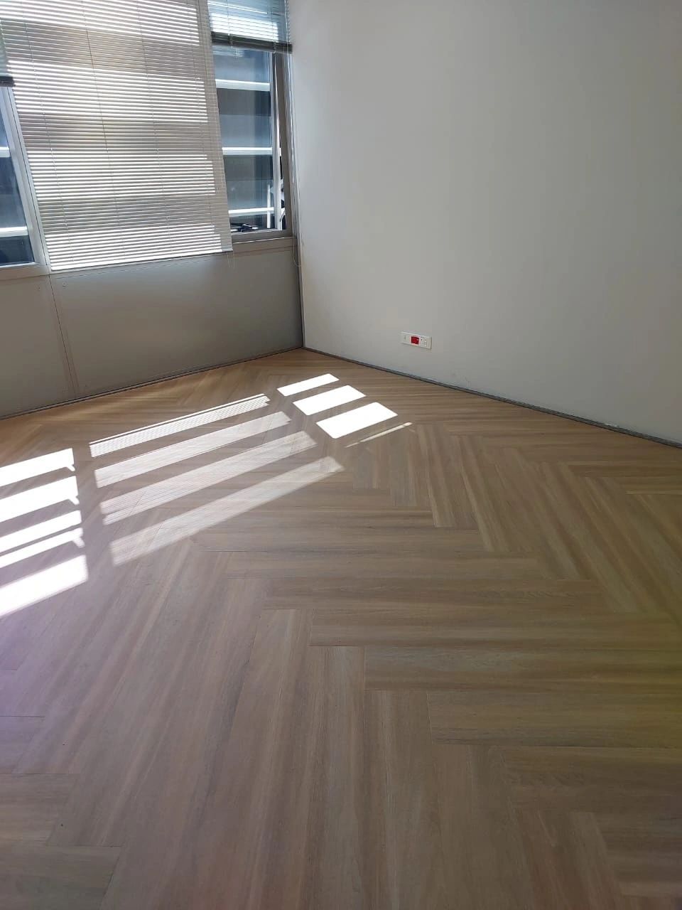 A sunlit office with a pale oak herringbone vinyl floor