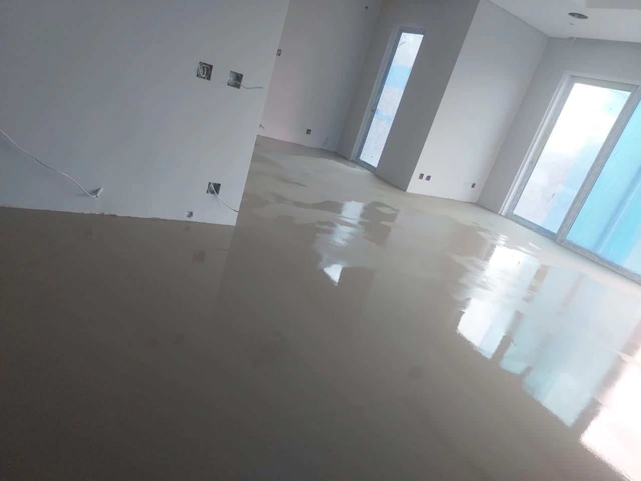 A newly screeded room with the wet floor reflecting the windows