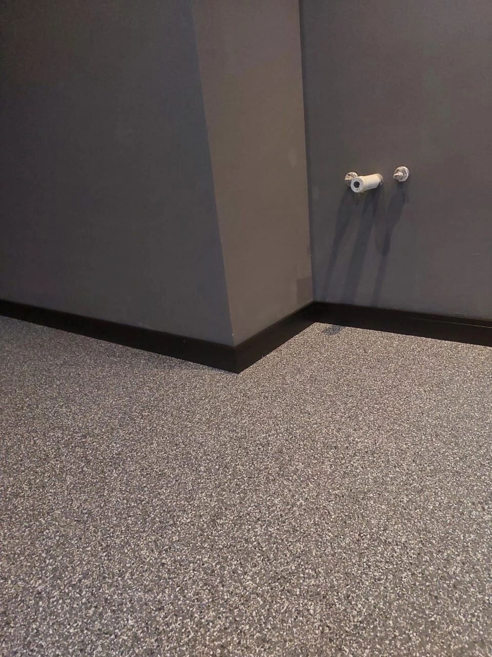Speckled grey vinyl floor meeting a dark wall and black skirting